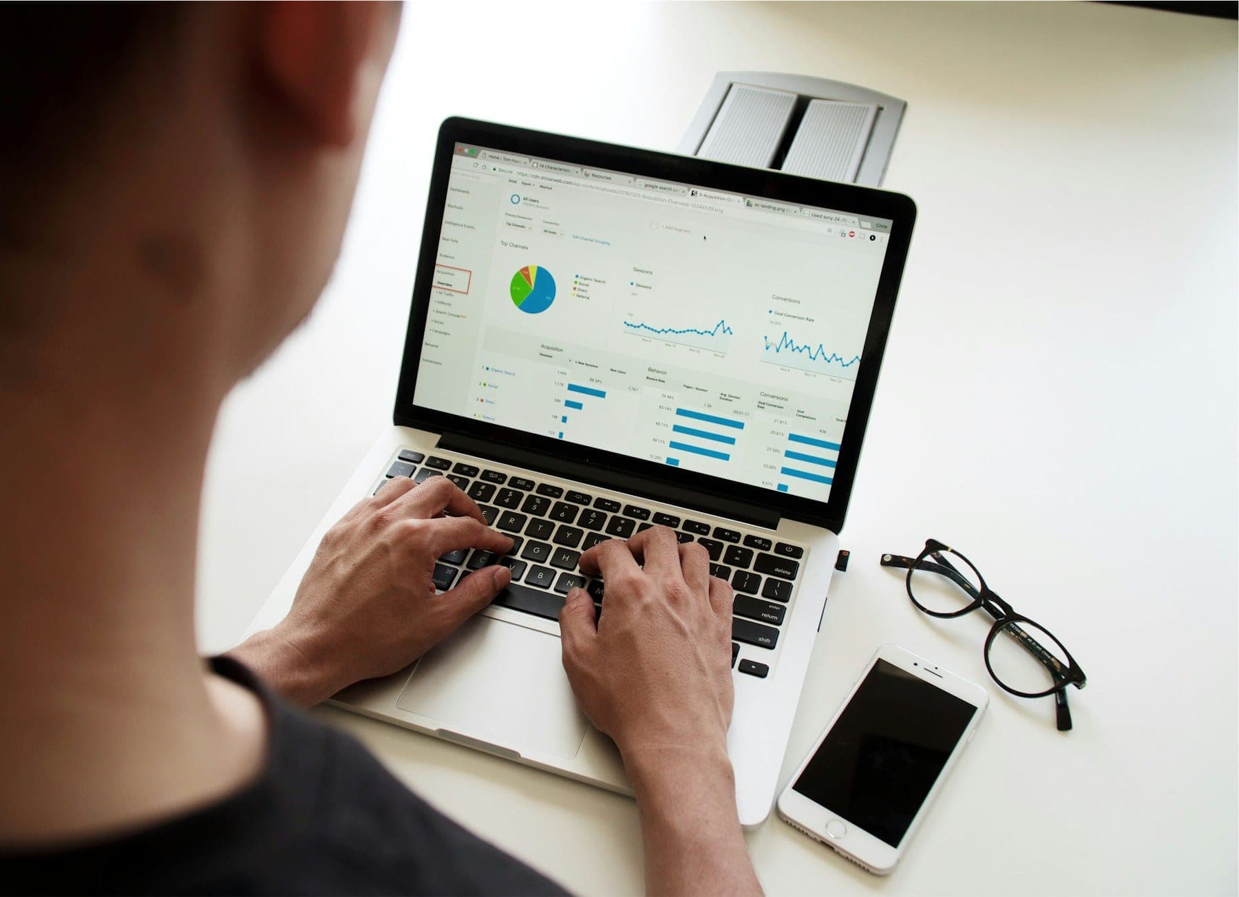 A laptop on a desk showing financial charts, beside a notebook and glasses.