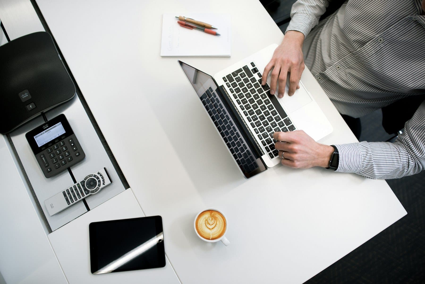 An organised desk seen from above with a laptop, telephone and coffee.