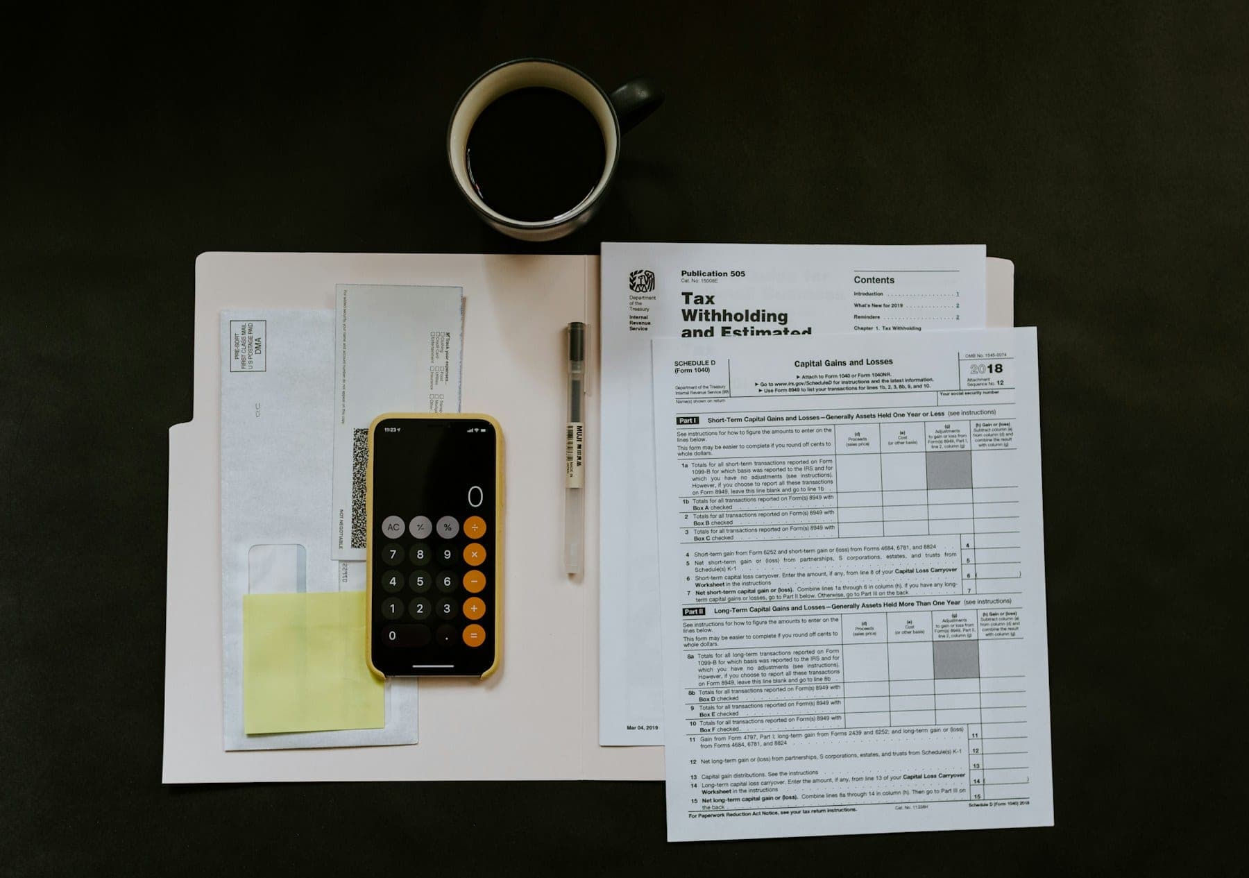 Tax return forms, a calculator and a cup of coffee arranged on a dark desk.